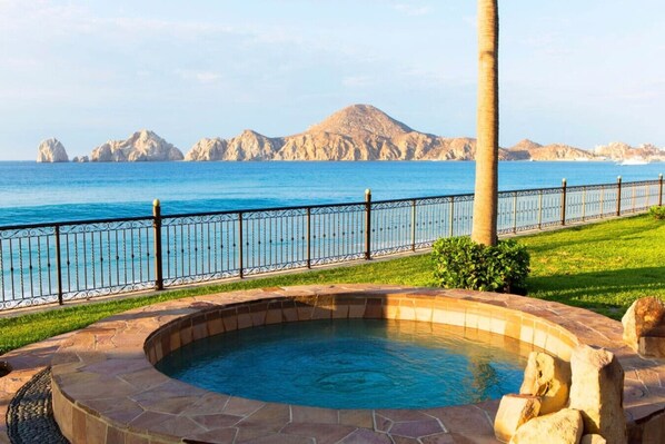 Una piscina con borde de piedra, cerca metálica y vistas al mar y las montañas.