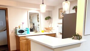 A modern kitchen with a central island, wooden cabinets, a microwave, and a refrigerator. - Remodeled basement in Corvallis, surrounded by forest and trails! (Corvallis)