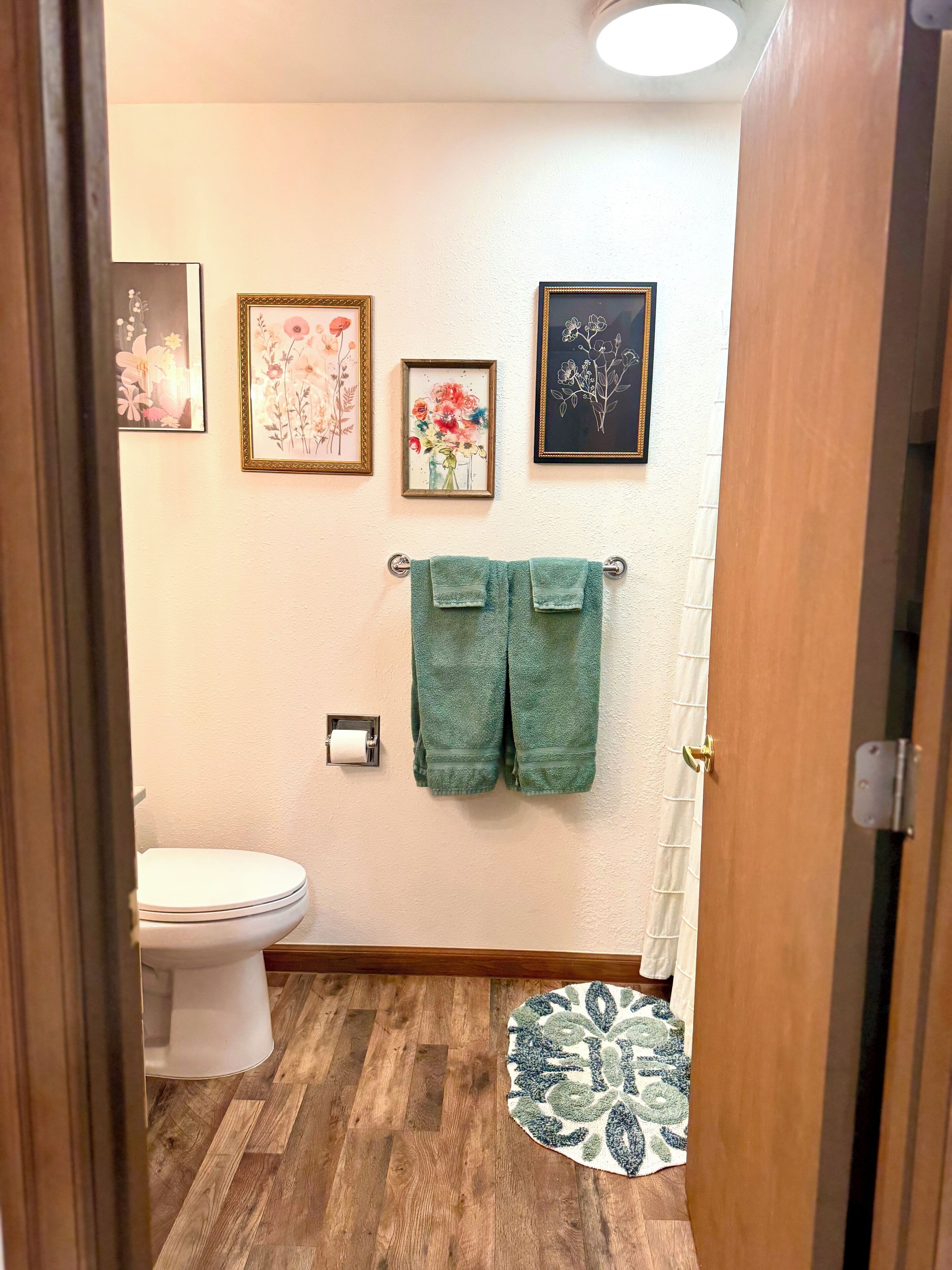 Ein Badezimmer mit Toilette, grünen Handtüchern und drei gerahmten Blumenbildern an der Wand.
