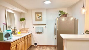 A compact kitchen with wooden cabinets, a built-in microwave, a stainless steel refrigerator, and a small sink. - Remodeled basement in Corvallis, surrounded by forest and trails! (Corvallis)