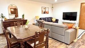A living room with a dining table, sofa, TV, and wooden flooring. - Remodeled basement in Corvallis, surrounded by forest and trails! (Corvallis)