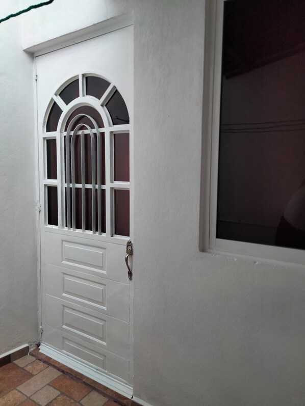 Una puerta blanca con ventanal y reja de metal.