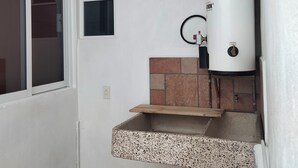 Une petite salle de bain avec un lavabo blanc, une fenêtre et un chauffe-eau fixé au mur.