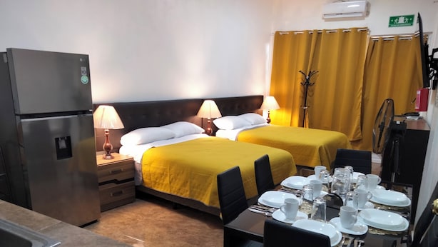 Une chambre d’hôtel avec deux lits, une table à manger dressée pour deux personnes, un réfrigérateur et un petit coin cuisine.
