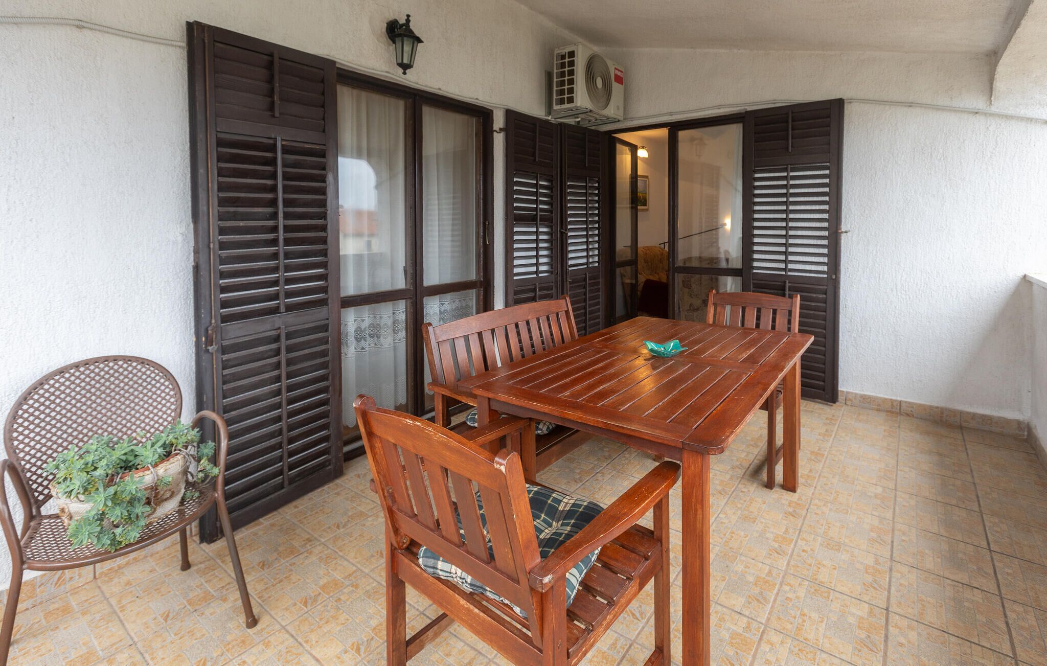 A wooden table with four chairs, a wicker chair with a plant, and a tiled floor.