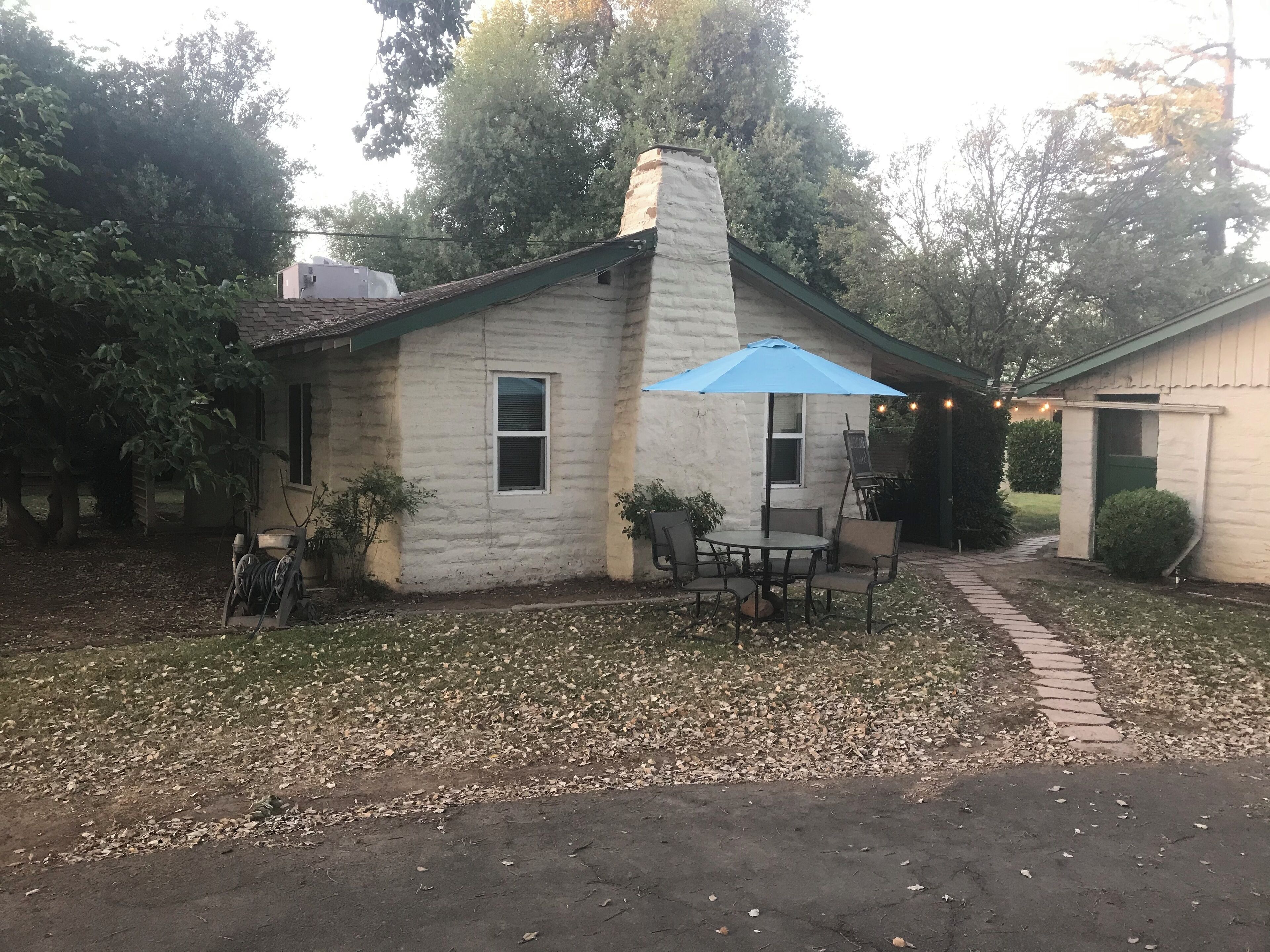 Une petite maison dotée d’un patio comprenant une table et des chaises, un parasol bleu et un chemin de briques menant à la maison.