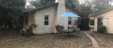 Une petite maison dotée d’un patio comprenant une table et des chaises, un parasol bleu et un chemin de briques menant à la maison.