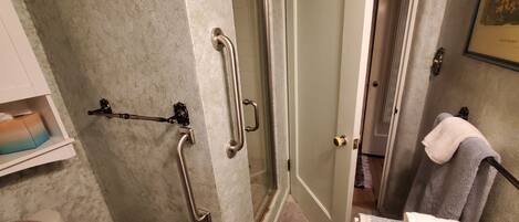 A bathroom with a shower, grab bars, a towel rack, and a toilet.