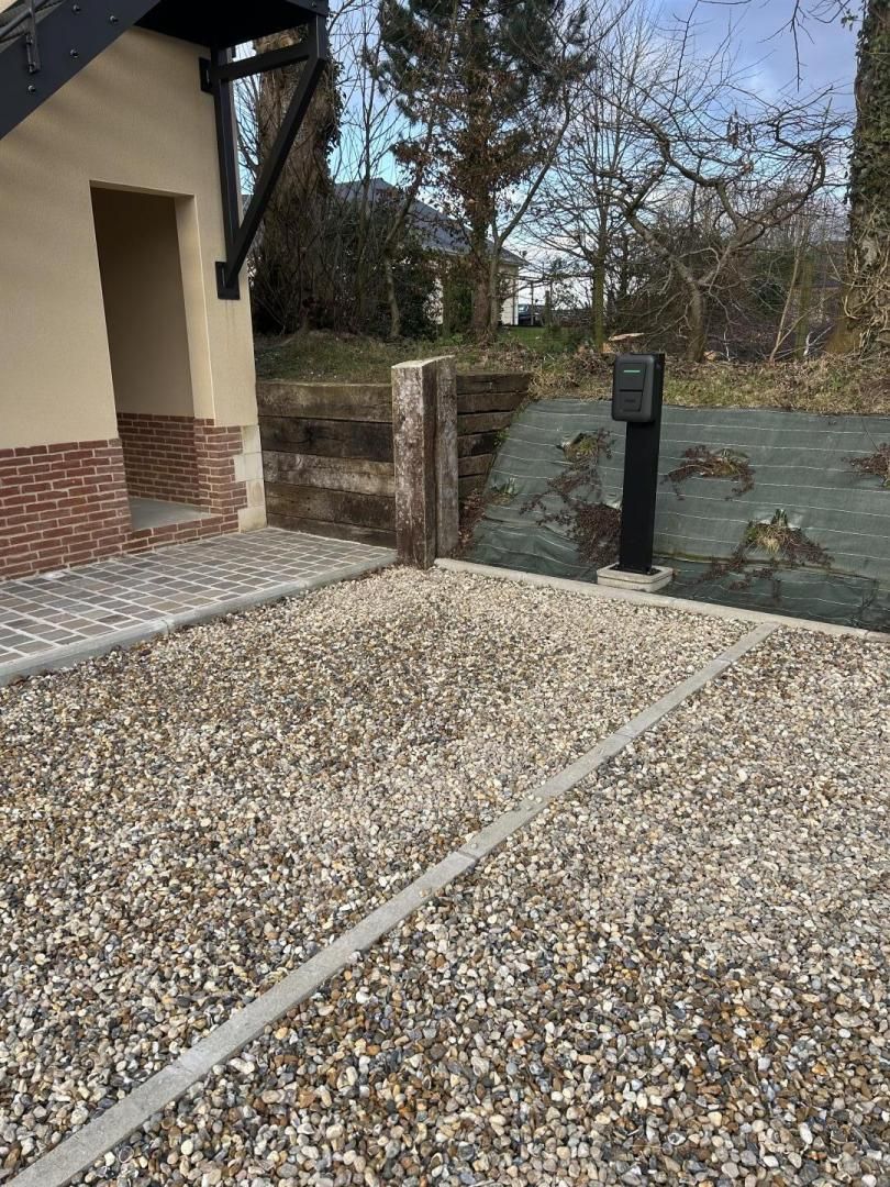 Een grindpad dat leidt naar een gebouw met een bakstenen fundering en een metalen constructie aan de linkerkant.