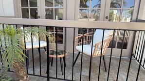 A balcony with a wrought iron railing, two wicker chairs with cushions, and a small table.