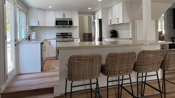 A modern kitchen with white cabinets, stainless steel appliances, and a bar area with wicker chairs.