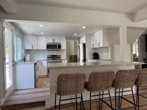 A modern kitchen with white cabinets, stainless steel appliances, and a bar area with wicker chairs.
