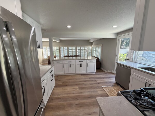 A modern kitchen with white cabinetry, a stainless steel refrigerator, a large island, and a gas stove.