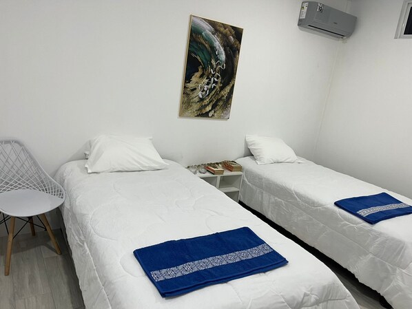 Una habitació amb dos llits, una cadira i un quadre a la paret.