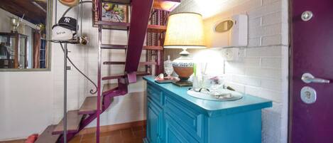 A room with a purple door, a blue cabinet, a staircase with purple railings, and a mirror with a hat on it.