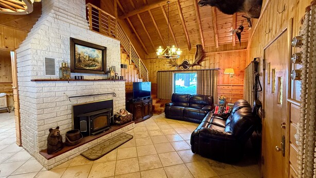 A log cabin interior with a fireplace, leather sofa, television, and a mounted deer head.