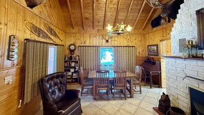 A wooden interior with a dining area, leather chair, wooden ceiling, chandelier, fireplace, and mounted animal heads.