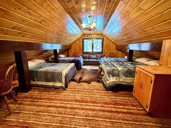 A cozy attic bedroom with two beds, a wooden ceiling, a large window, and a rustic decor.