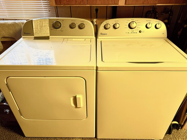 Vista frontal de un conjunto de lavadora y secadora Whirlpool blancos en un cuarto de lavado con gabinetes de madera arriba.