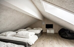 Ein modernes Schlafzimmer im Dachgeschoss mit schrägen Wänden, einem Bett mit weißer Bettwäsche, einem schwarzen Sitzsack und einem an der Wand befestigten Fernseher.