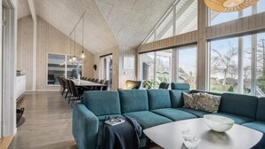 Un salon moderne avec un canapé de couleur turquoise, un coin repas doté d’une longue table et de grandes fenêtres offrant une vue sur l’extérieur.