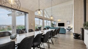 Un grand espace à manger avec une longue table et des chaises, un coin cuisine équipé d’une cuisinière et d’un évier, et une grande fenêtre donnant sur l’extérieur.
