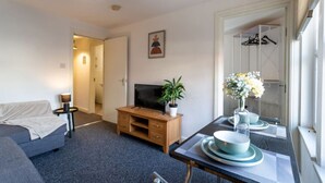 A modern hotel room with a sofa, a TV on a wooden stand, a dining table with a vase of flowers, and a mirror reflecting a wardrobe. - Contractor*Long Stays Discounts*Parking (Bristol)