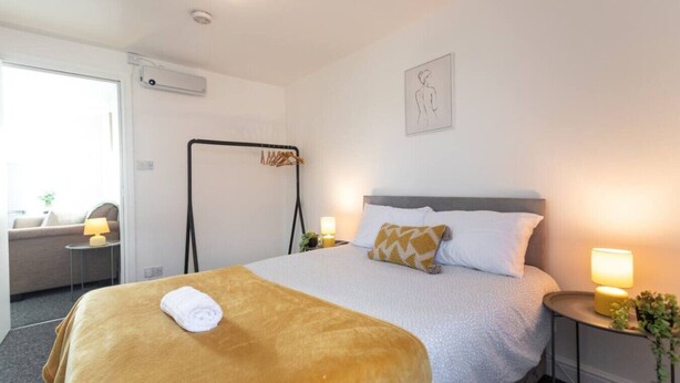 A hotel room with a bed, a bedside table with a lamp, a chair, and a large window.
