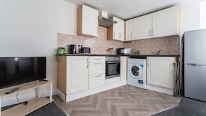 A compact kitchen with white cabinets, a washing machine, a microwave, and a refrigerator.