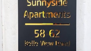 A black sign with gold lettering for Sunnyside Apartments, including the address 58-62 Belle View Road.