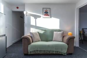 Ett litet, ombonat rum med en grön soffa, en lampa och en inramad tavla på väggen.