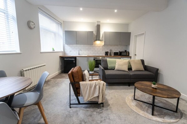 A modern kitchen with grey cabinets, a built-in oven, and a dining area with a round table and chairs.