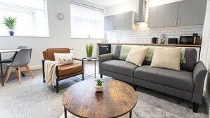 Una sala de estar moderna con un sofá gris, un sillón de cuero marrón y una mesa de centro de madera. Hay una mesita auxiliar con una planta.