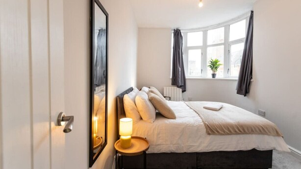 Un dormitorio con cama, lámpara de noche, ventana con cortinas y una planta en maceta.