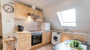 A compact kitchen with wooden cabinets, a built-in oven, a washing machine, and a small table with a plant. - Contractor*Long Stays Discounts*Parking (Bristol)