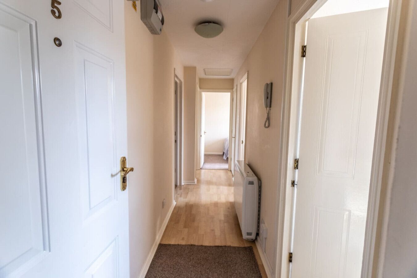 A narrow hallway with white doors, a radiator, and a phone on the wall.