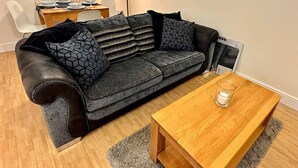 Ein modernes Wohnzimmer mit einem grauen Sofa, einem Holztisch und einem Esstisch mit Tellern und Gläsern.