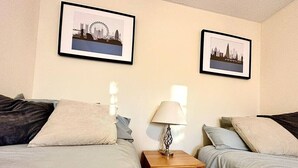 Ein Hotelzimmer mit zwei Betten, einem Nachttisch mit Lampe und zwei gerahmten Bildern an der Wand.