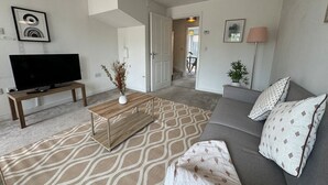 A modern living room with a flat-screen TV, a wooden coffee table, a patterned rug, a grey sofa, and a lamp. - Bolehyde House Long Stay Discounts Free Parking (Swindon)