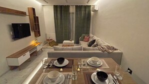 Ett modernt vardagsrum med en matplats för två personer, med ett träbord, två soffor, en platt-TV och en inbyggd hylla.