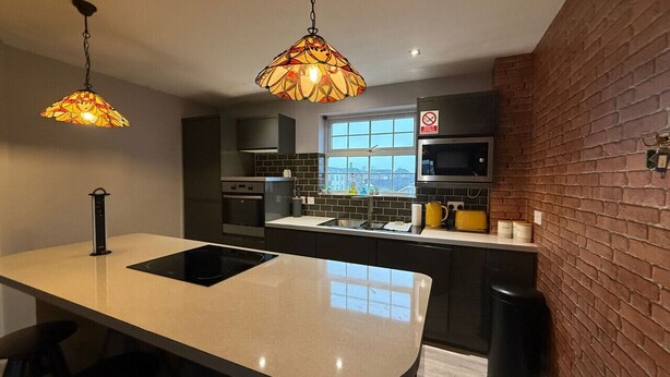 A modern kitchen with a central island, a hanging light fixture, and a brick accent wall.
