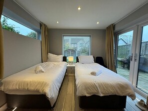Two single beds with white linens and lamps, overlooking a scenic view through a sliding glass door.