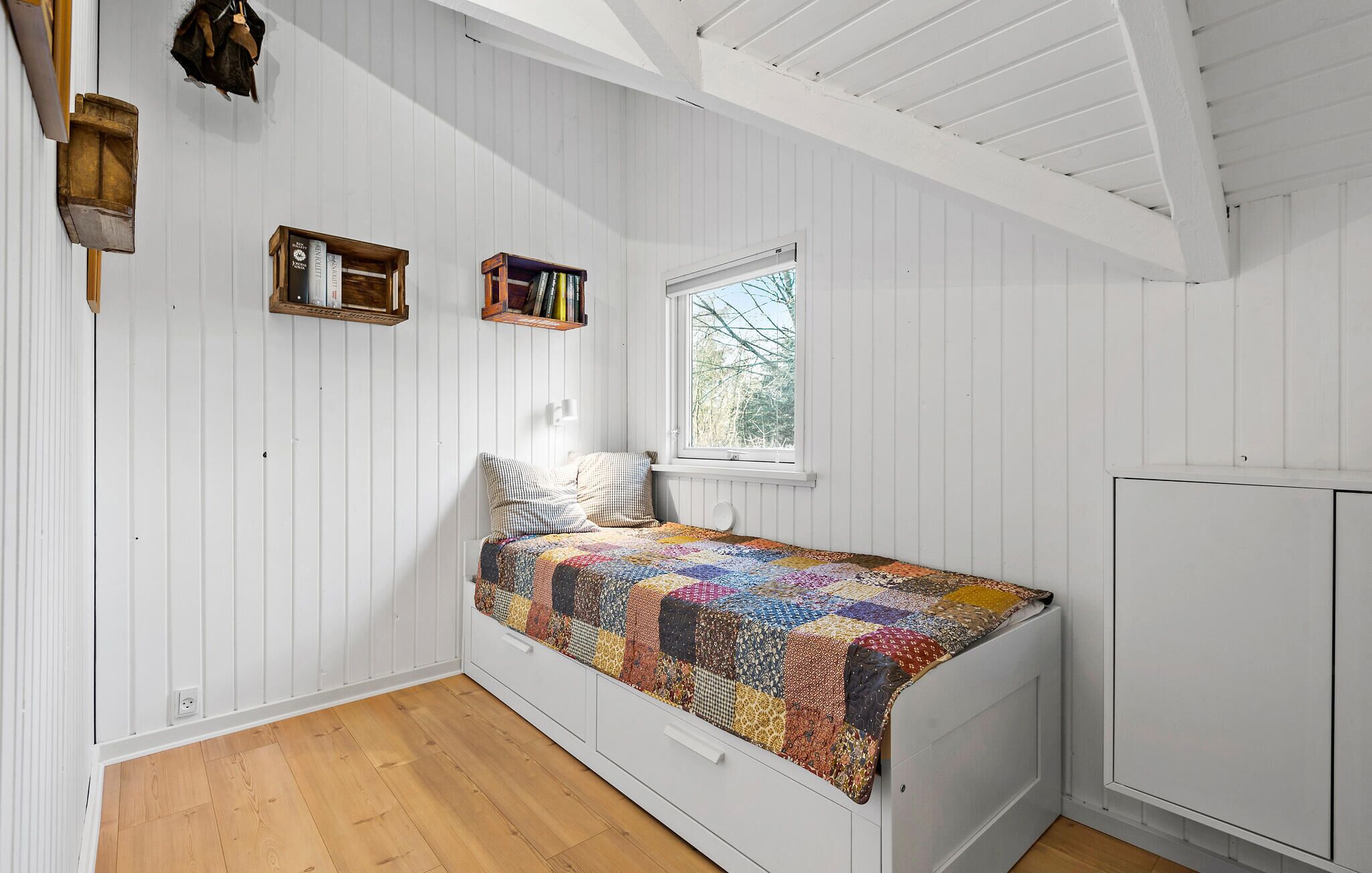 Une chambre avec un lit en bois, une fenêtre et des étagères intégrées.