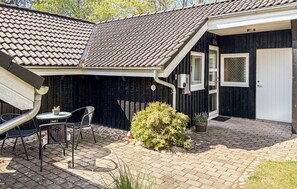 Un bâtiment noir avec un toit recouvert de tuiles, une porte et un petit patio comprenant une table et des chaises.