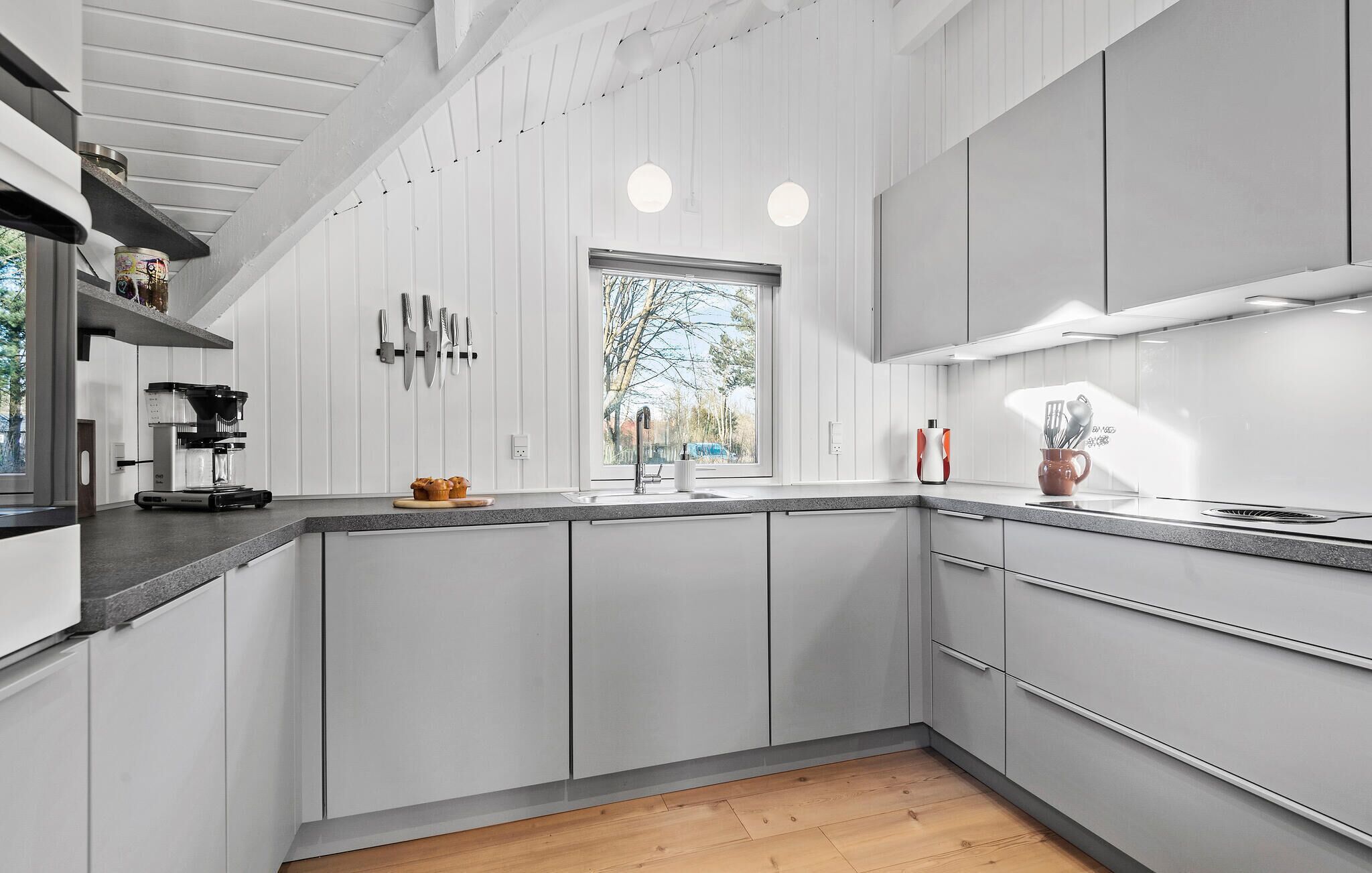 A modern kitchen with white cabinetry, a built-in oven, and a large window providing natural light.