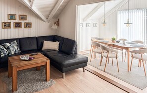 A modern living room with a black leather sofa, a wooden coffee table, and a dining area with a round table and chairs.