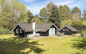 A cabin with a large deck, a dining area, and a separate building with a chimney.