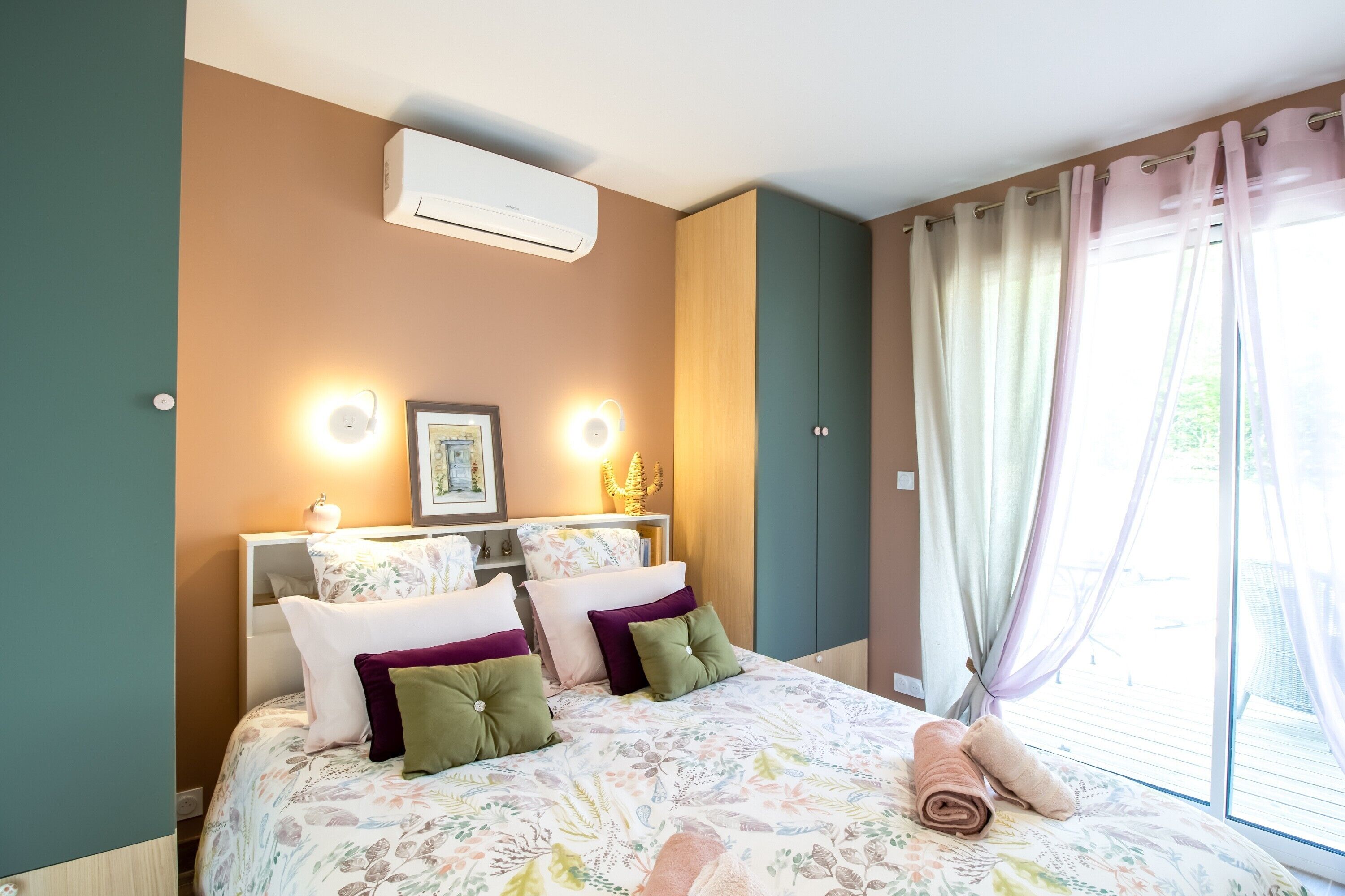 Une chambre à coucher avec un lit, des oreillers, des lampes de chevet, un climatiseur et une fenêtre avec des rideaux.