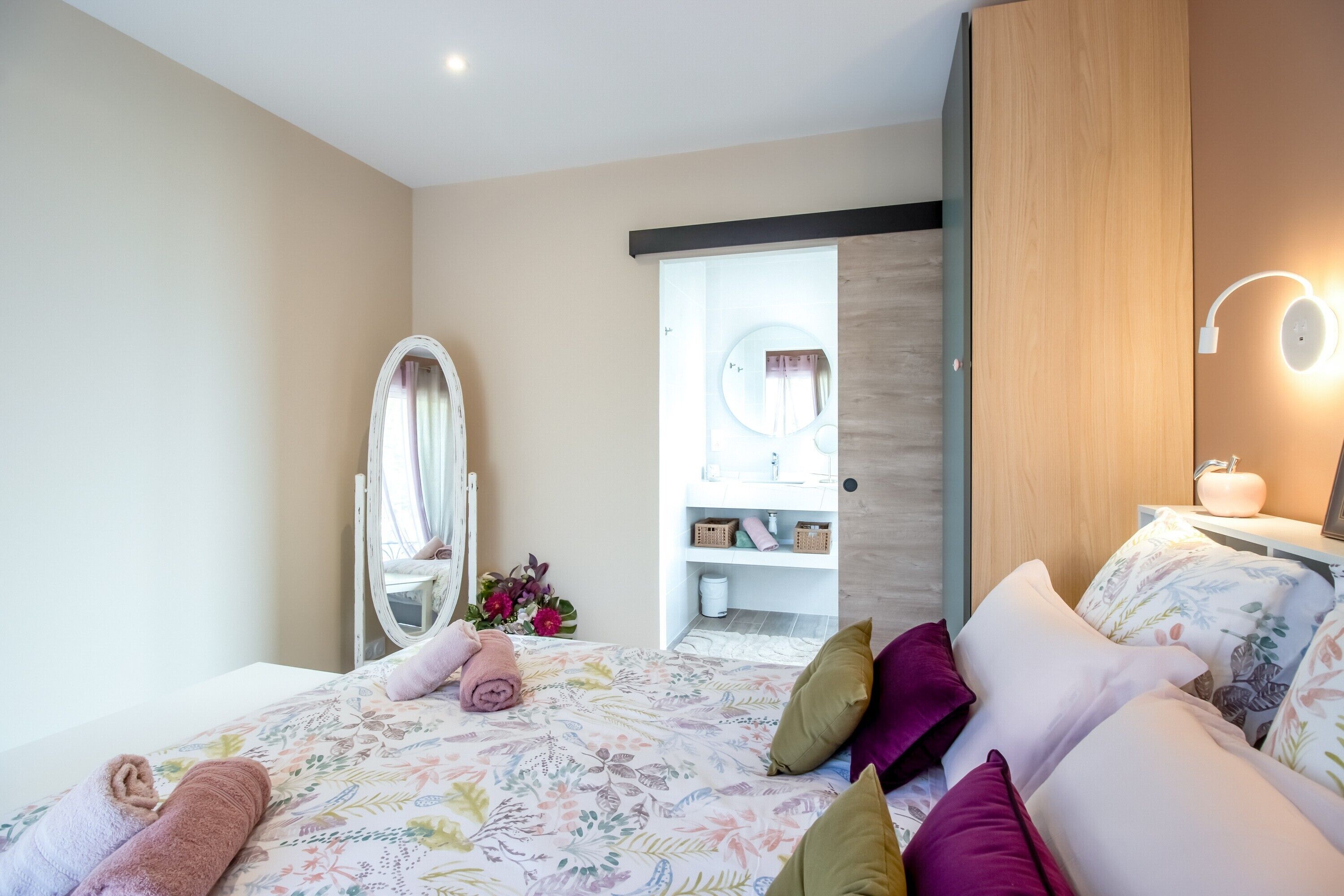 Un dormitorio con cama, espejo, mesita de noche con lámpara y puerta que da a un baño.