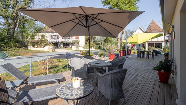 A wooden deck with outdoor furniture, a large umbrella, and a view of the surrounding area.